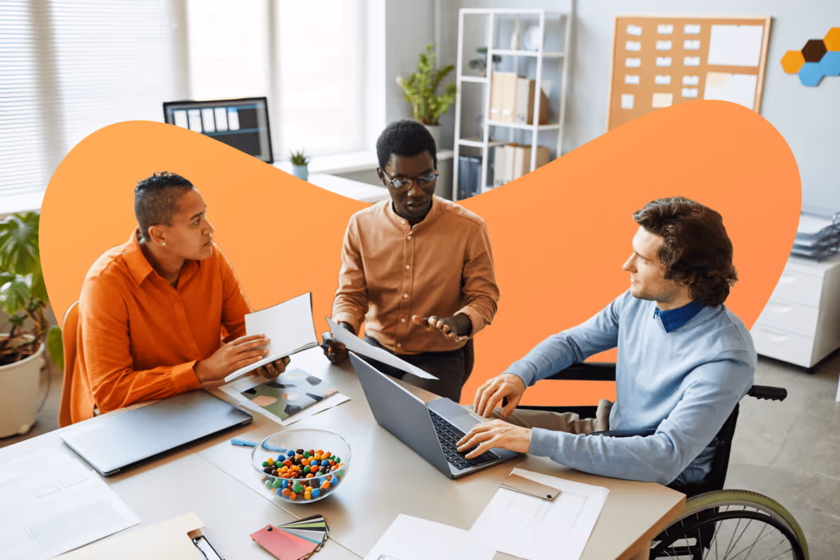 Three diverse people in a modern office having a discussion with documents and laptop on the table, one person is in a wheelchair.