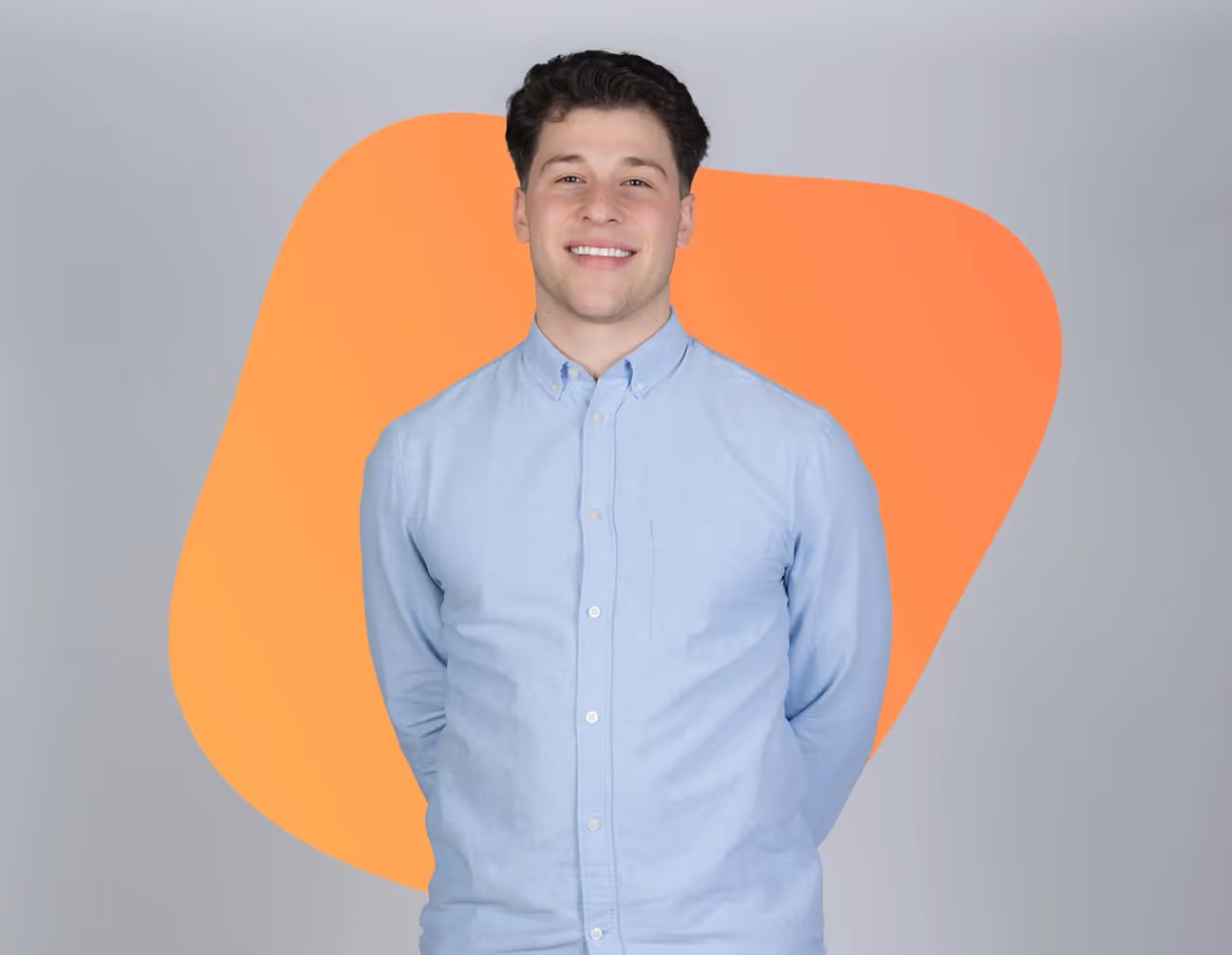 Young man with dark hair wearing a light blue button-up shirt, smiling against a gray background with an orange abstract shape.