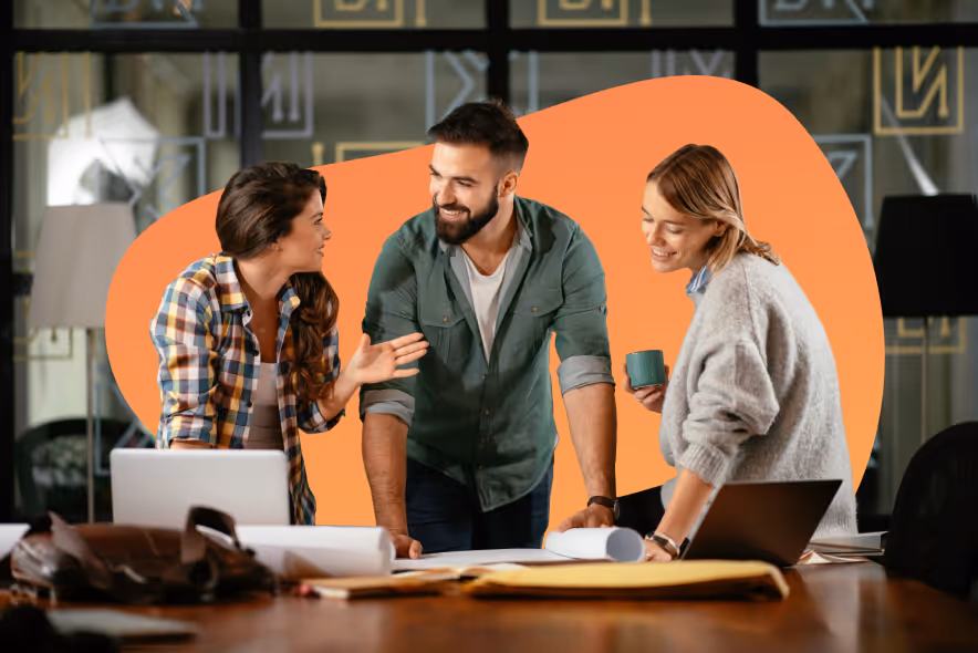 Three colleagues engaged in a lively discussion around a table with laptops and documents in a modern office.