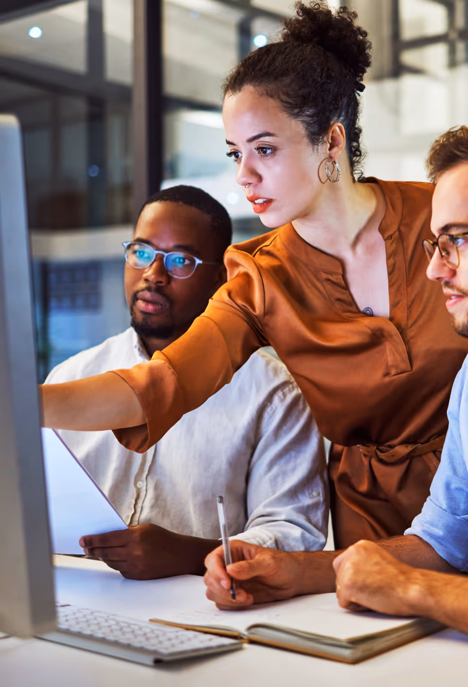 Three colleagues collaborating and discussing work while looking at a computer screen in an office.
