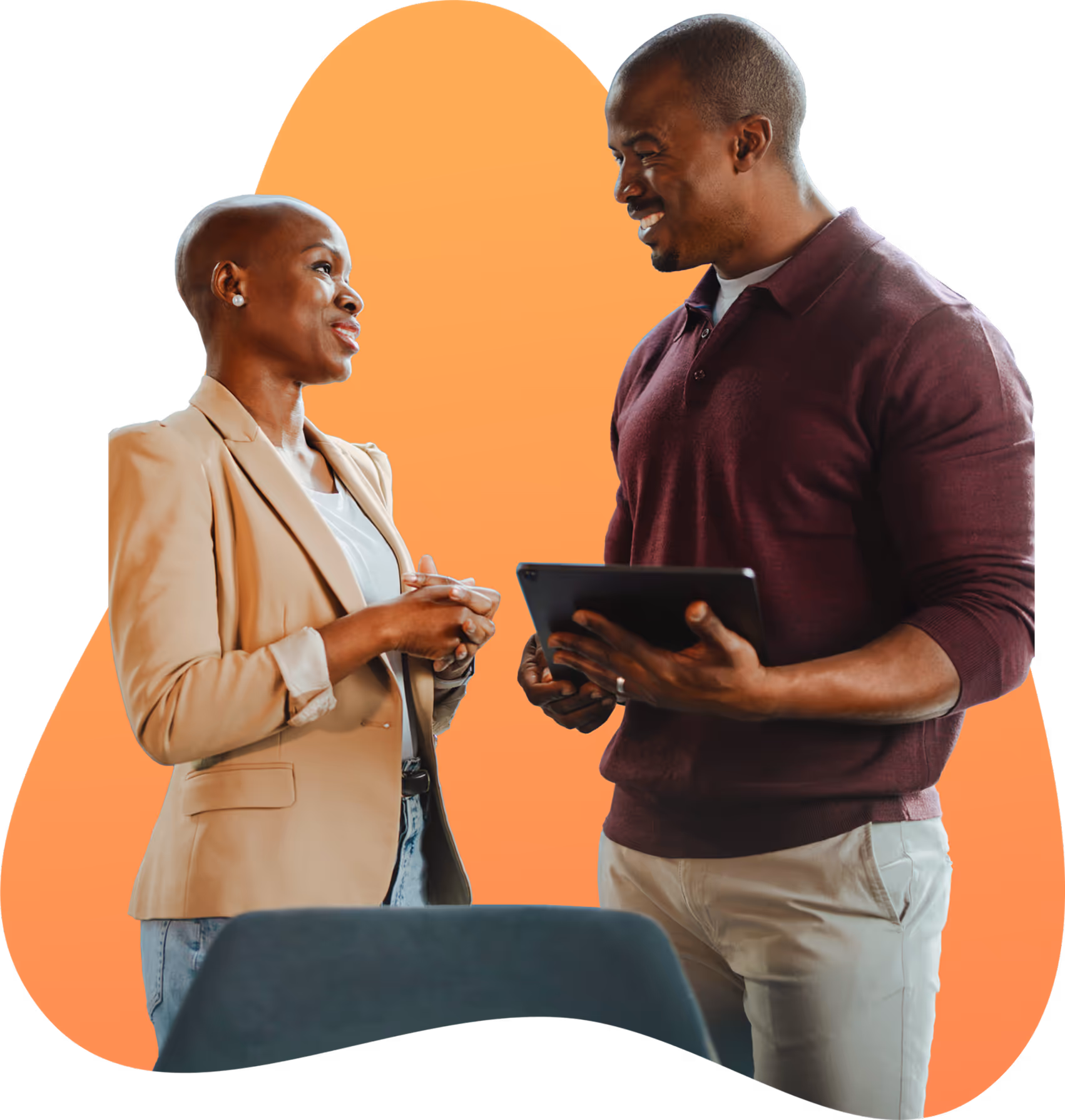 Two colleagues smiling and having a discussion, one holding a tablet, with an orange abstract background.