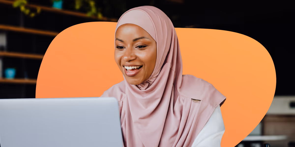 Smiling woman wearing pink hijab looking at a laptop screen with an orange abstract background.