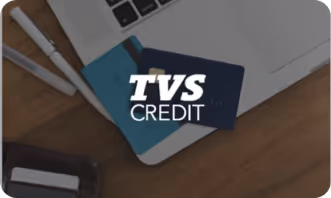 Laptop keyboard with two pens and two credit cards on top, with TVS Credit logo overlay.