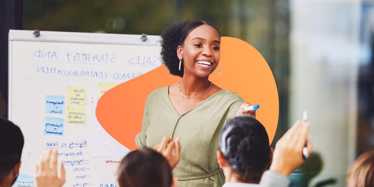 Smiling woman leading a presentation and holding a marker while attendees raise their hands.