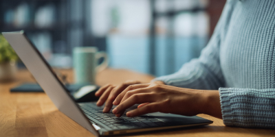 Hands typing on a laptop beside a coffee mug