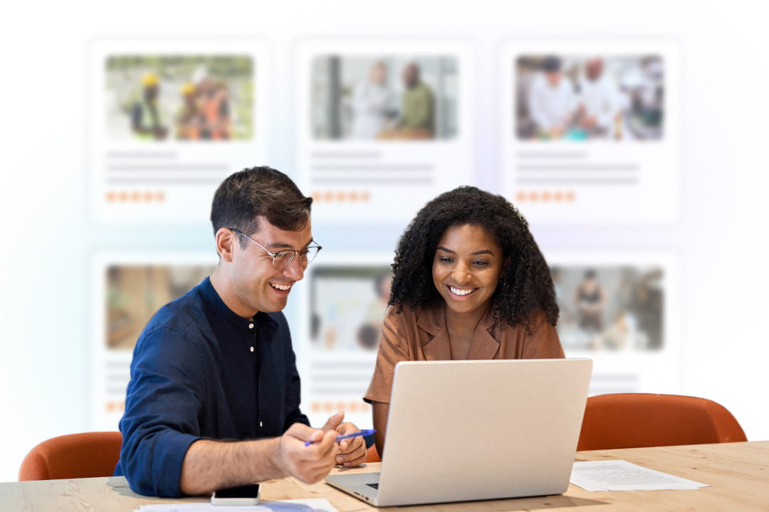 Two colleagues smiling at a laptop in front of course cards