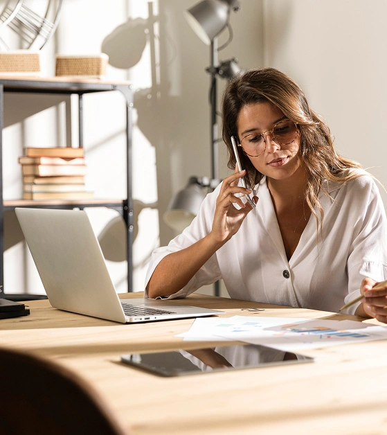 Young woman in eyeglasses is talking on the phone at the office