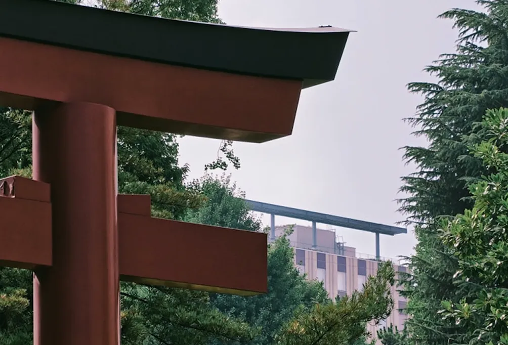 Close-up of a Torii gate with modern buildings in the background.