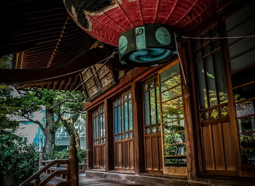A lantern hanging above a wooden house in a lush, green setting.