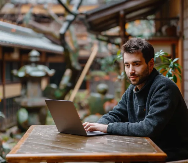 Man working on a laptop at an outdoor wooden table in a traditional setting