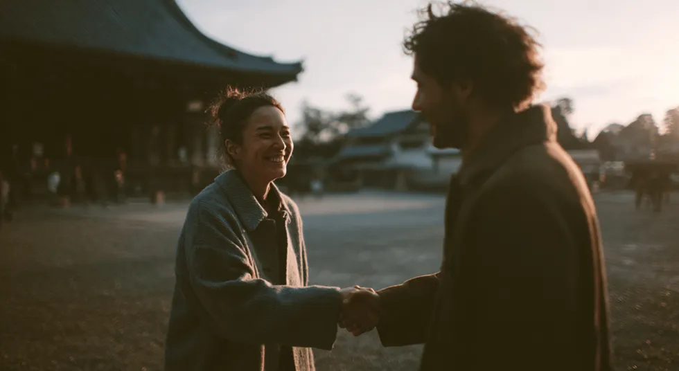 Two people shaking hands in front of a large temple structure