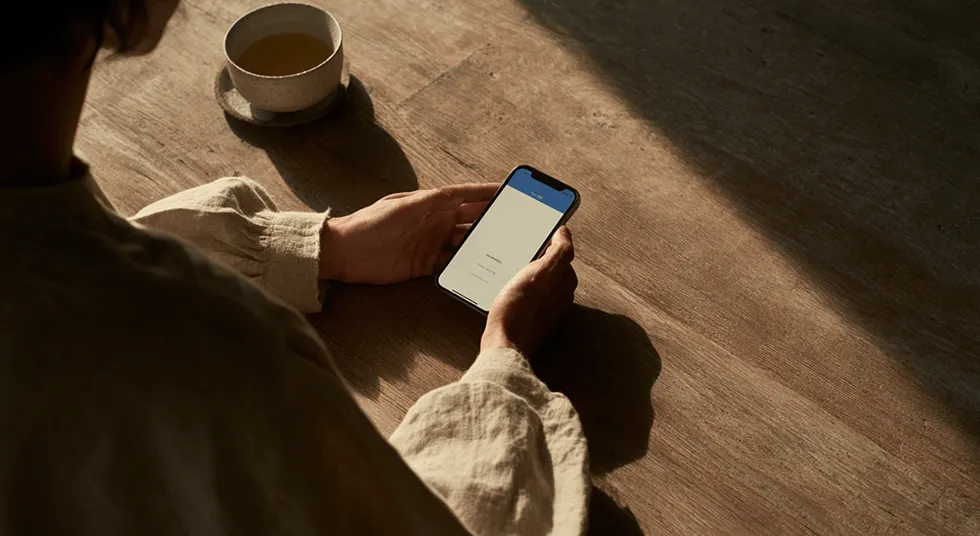 Person holding a smartphone at a wooden table with a cup of tea