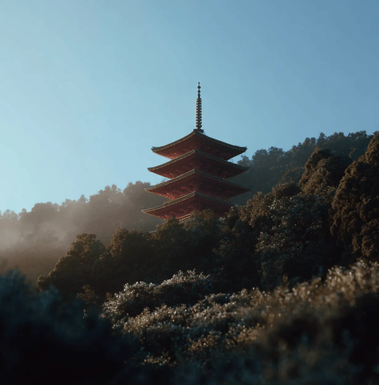Red pagoda rising above forested hills at sunrise