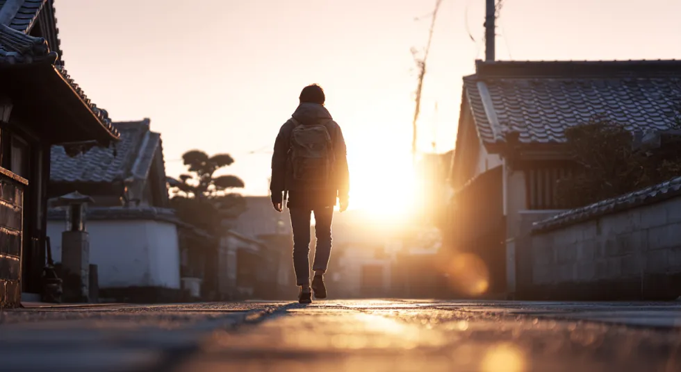 Person walking down a quiet street at sunrise.