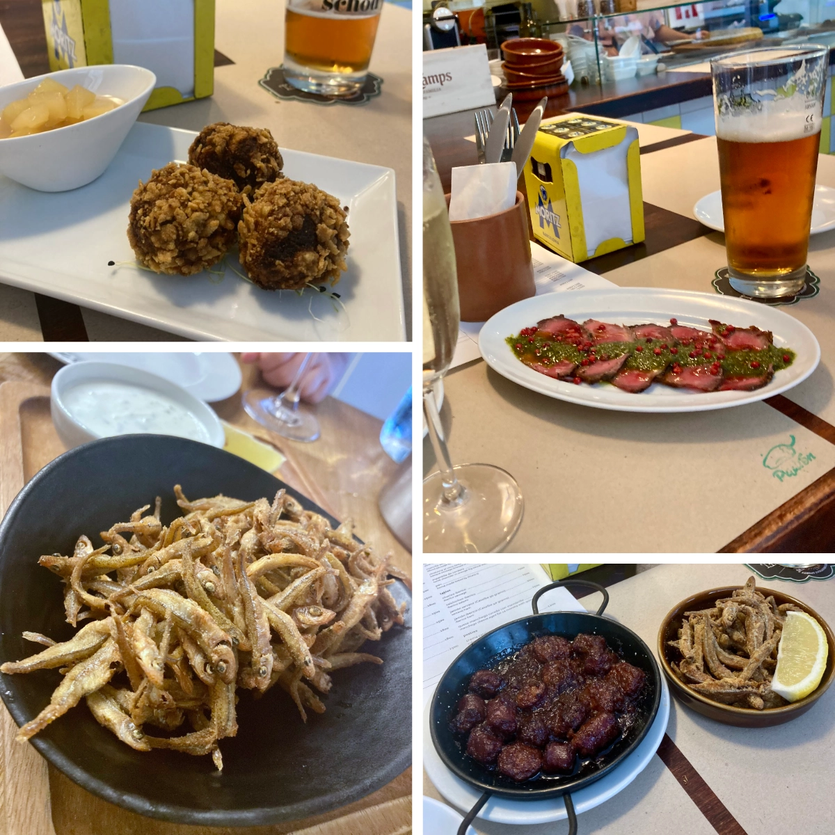 A table of Spanish-style tapas: fried bites and croquettes, crispy small fish (boquerones), sliced meat with green sauce, and a glass of beer, served across several small plates at a bar table.