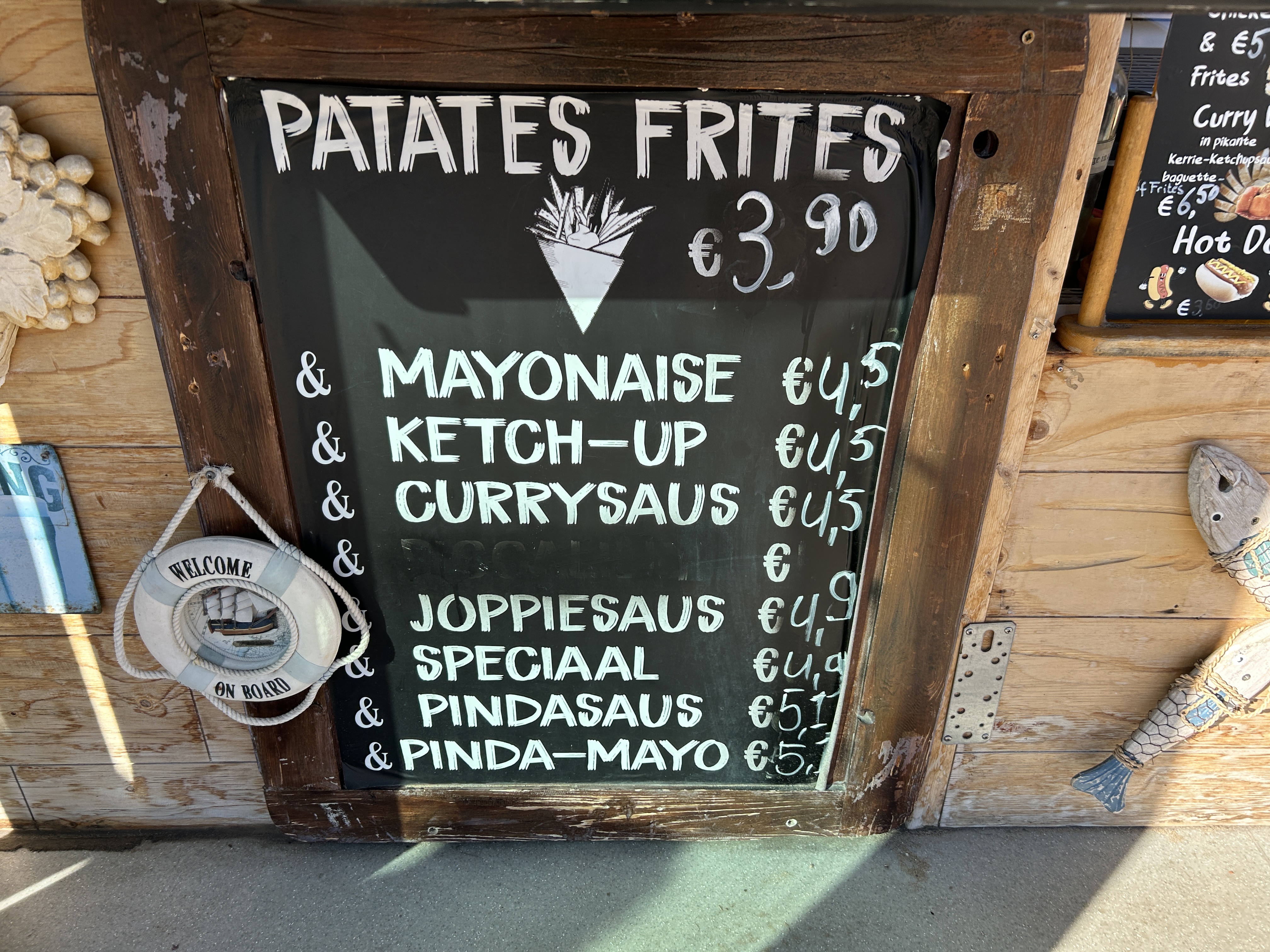 Chalkboard menu listing patates frites with sauce options including mayonnaise, ketchup, curry sauce, joppiesaus, speciaal, and peanut sauce, with prices in euros.