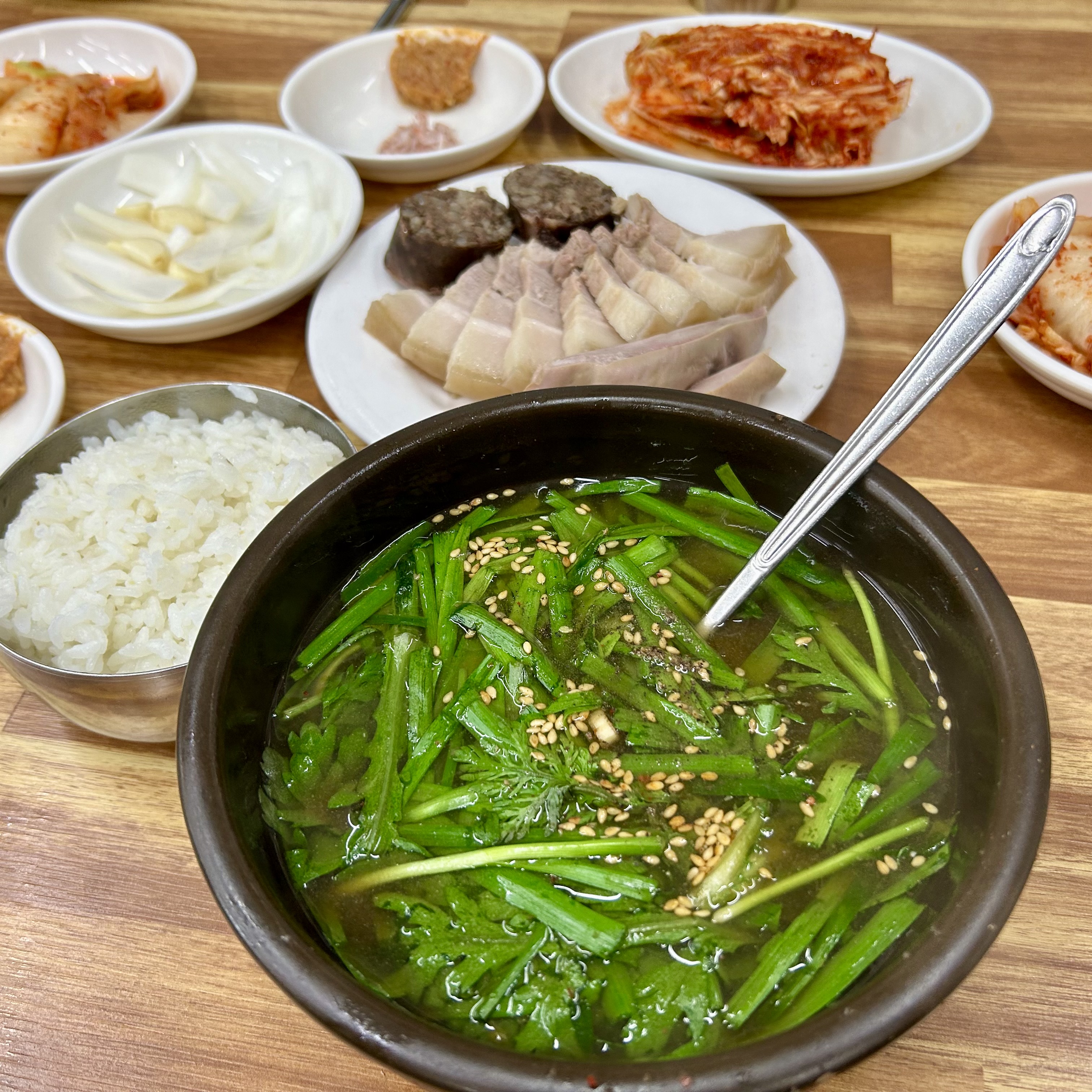 Korean sundae-guk soup topped with chives (buchu), with offal and meat pieces hidden beneath, served with rice and side dishes.