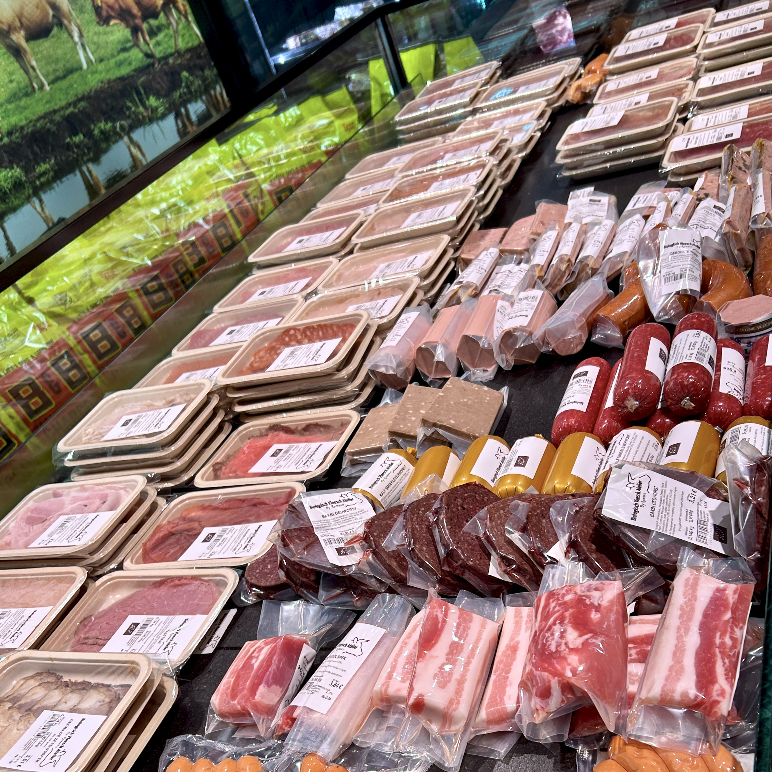 Packaged meats and sausages displayed in a local Italian butcher shop, showing a variety of cuts with images of cows in the background.