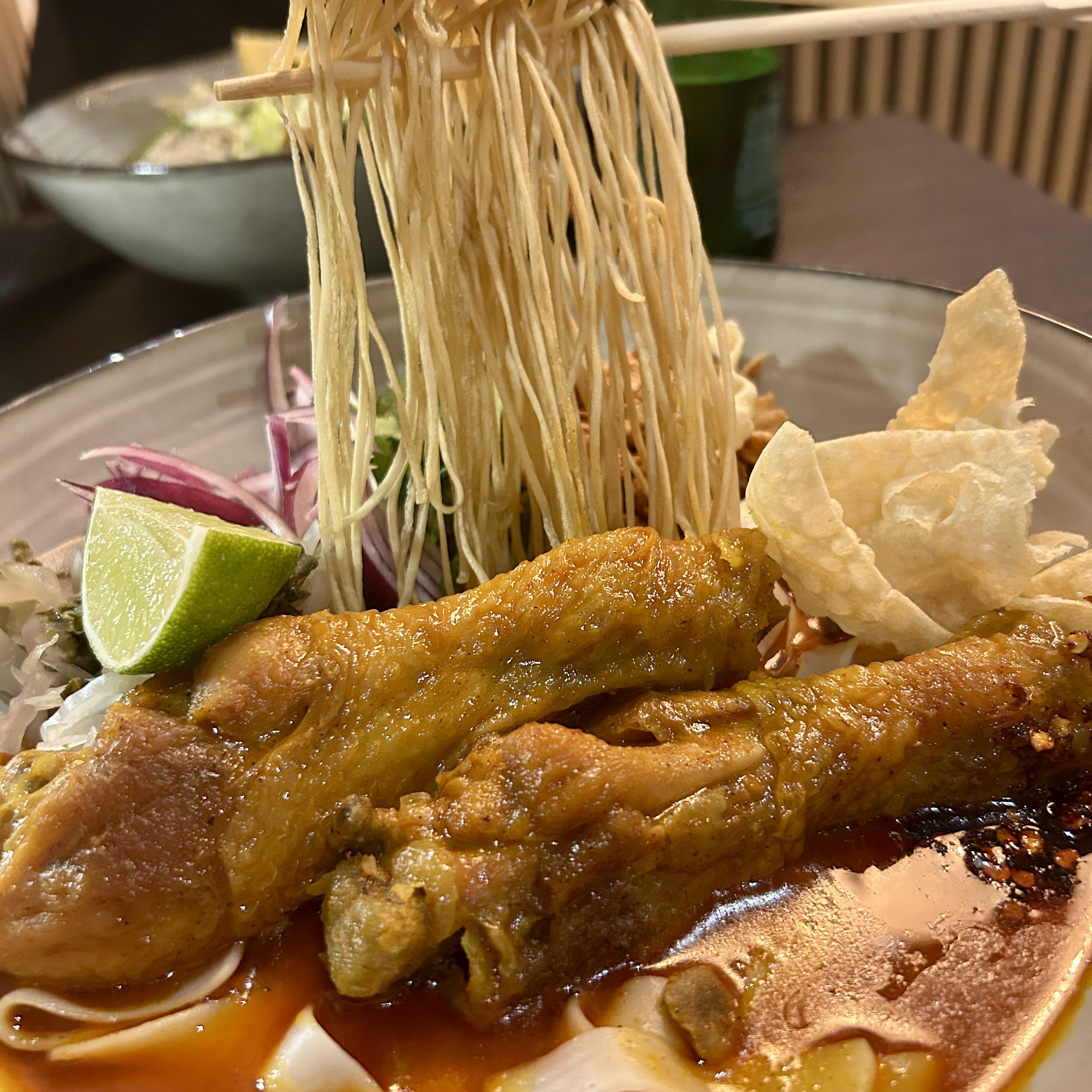 Northern Thai khao soi gai with bone-in chicken in curry broth, topped with crispy noodles and served with lime and garnishes.