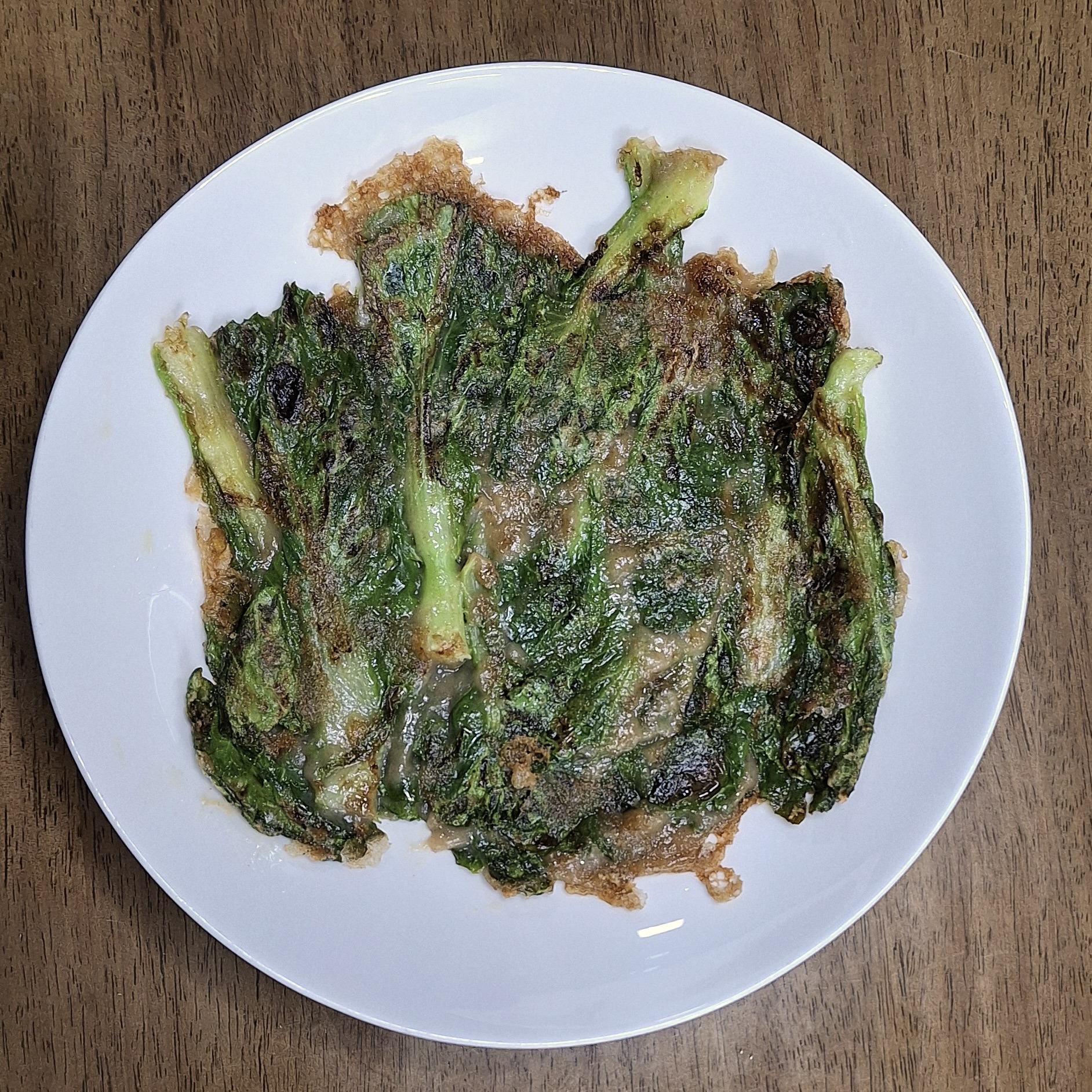A white plate with pan-fried bomdong jeon, the spring cabbage leaves charred at the edges and bound in a thin buckwheat batter.