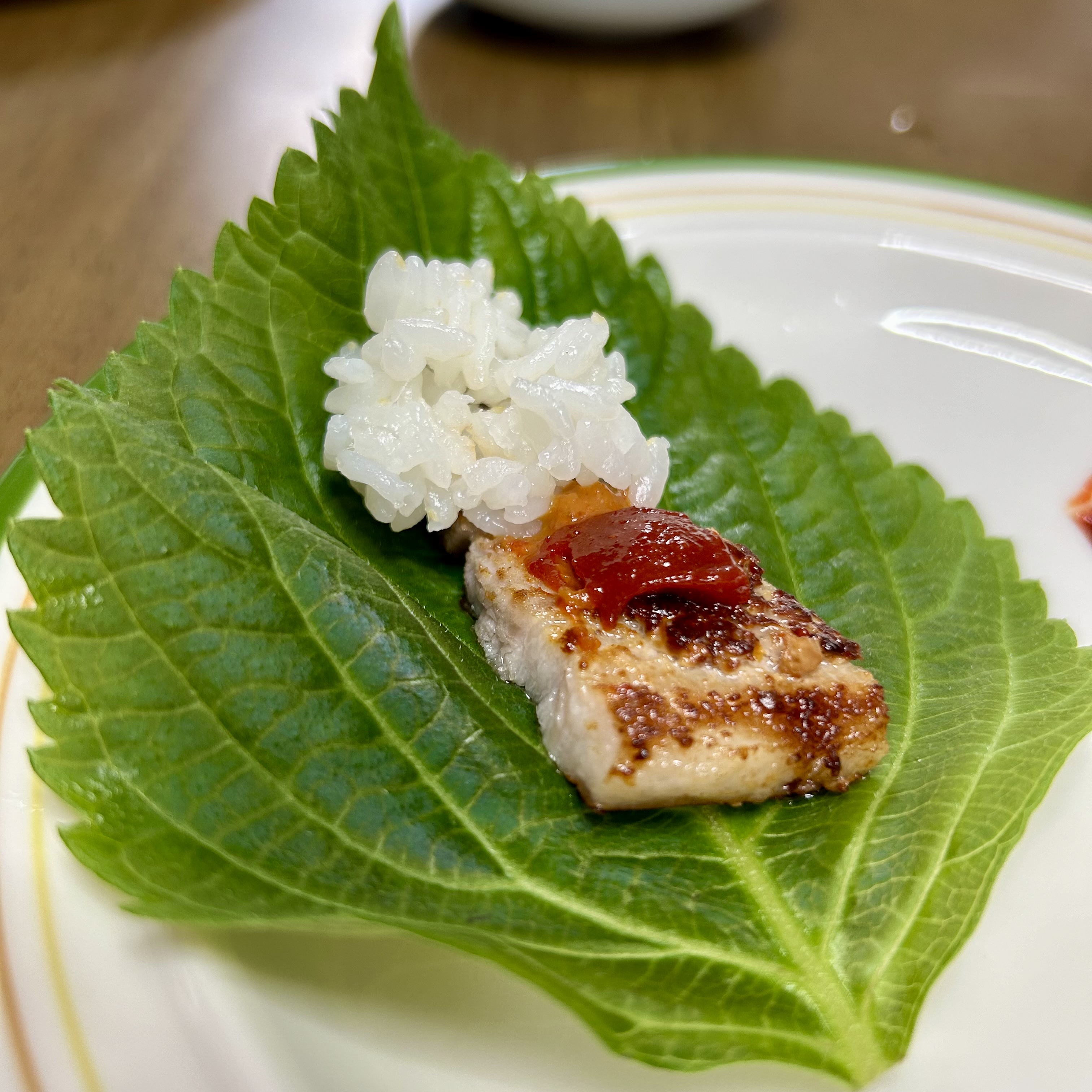 A perilla leaf holding a small mound of rice, a piece of grilled meat, and a dollop of ssamjang, ready to be wrapped and eaten.