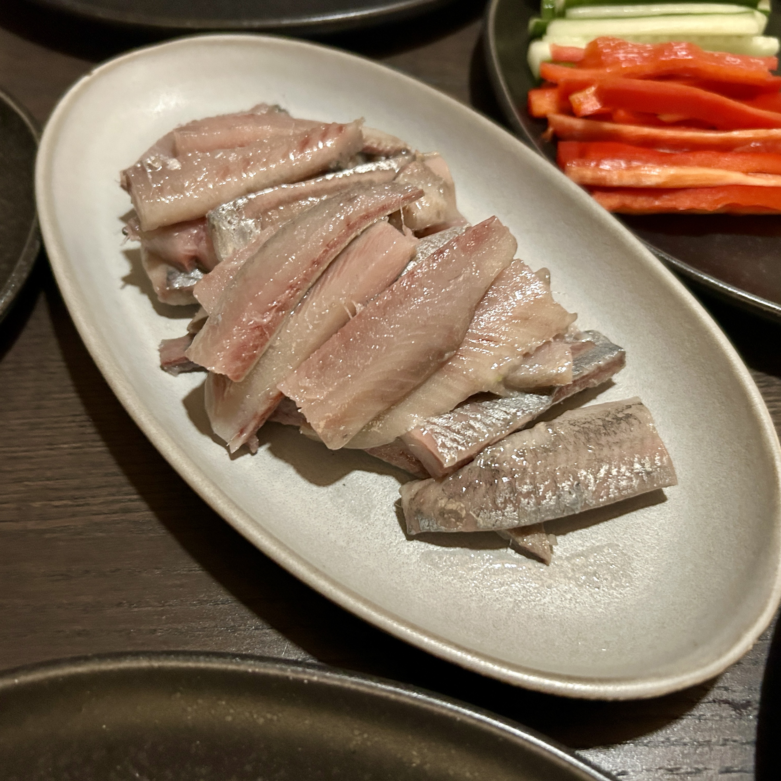 A table with plates of sliced raw herring, julienned vegetables.
