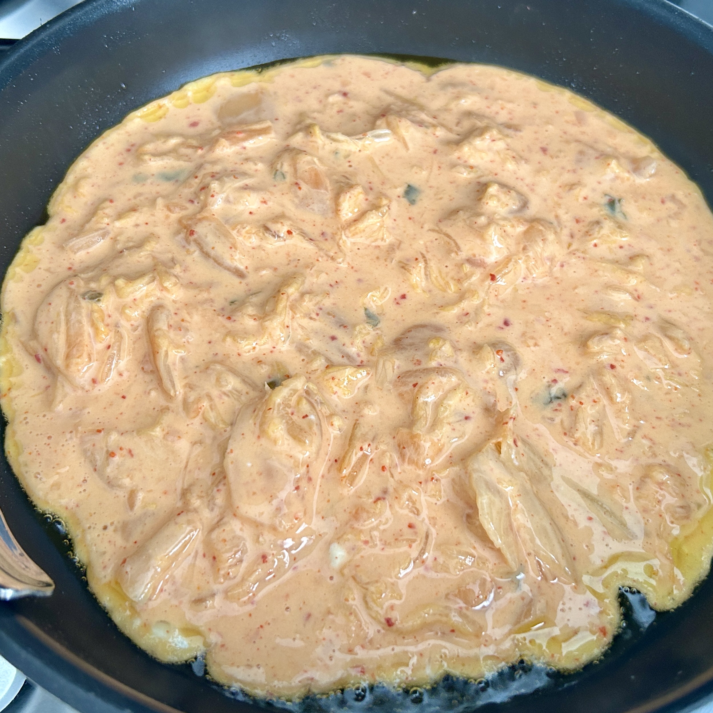 A large pan of kimchi buchimgae batter sizzling on the stovetop, still raw in the center, with the edges beginning to set.