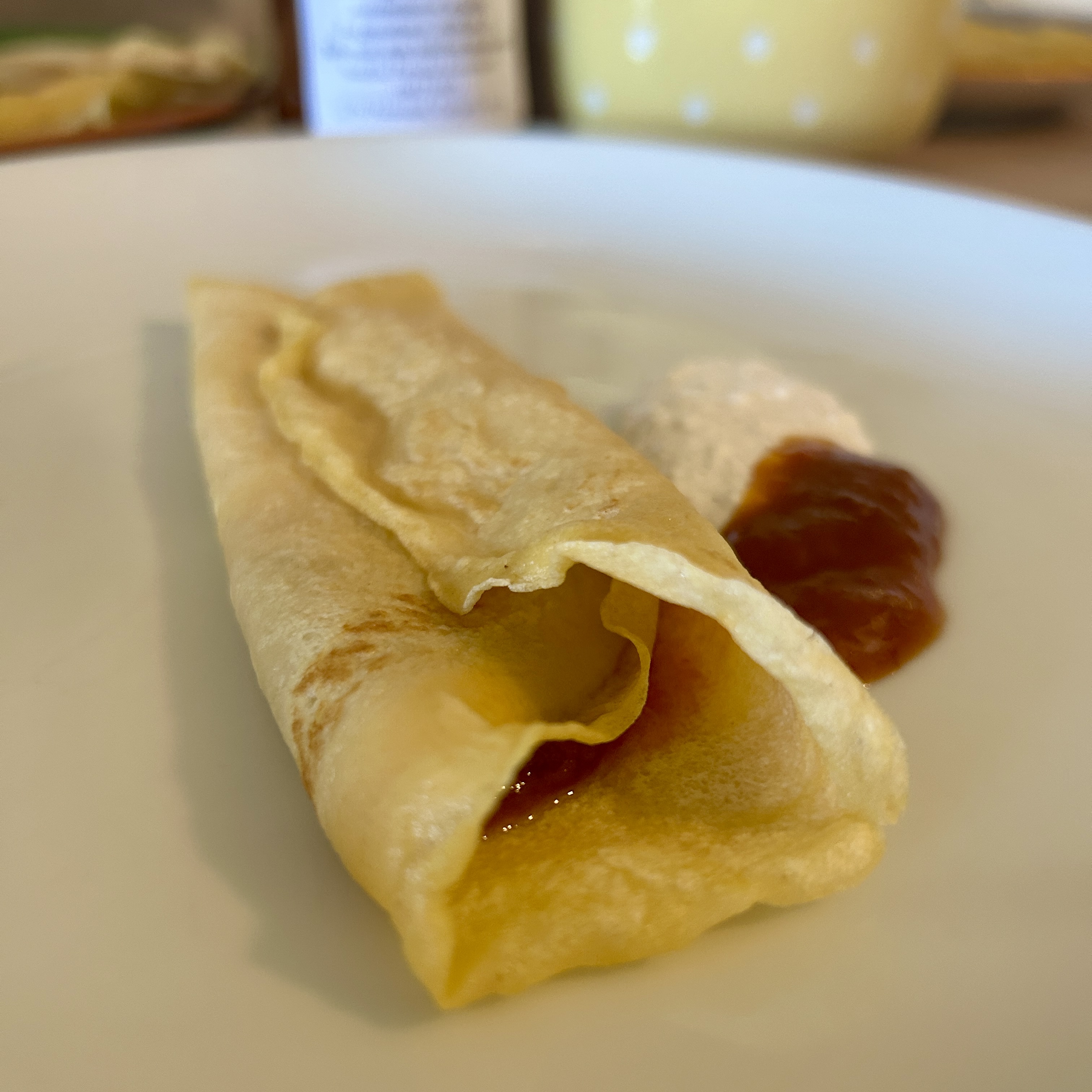 Thin rolled palacsinta on a white plate, filled with apricot lekvár, with a dollop of preserve on the side.