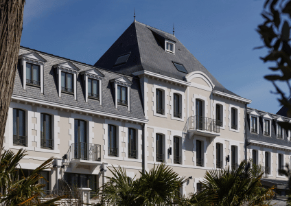 Façade classique en pierre du Grand Hôtel de Courtoisville à Saint-Malo, avec mansardes, balcons et terrasse ombragée de palmiers.
