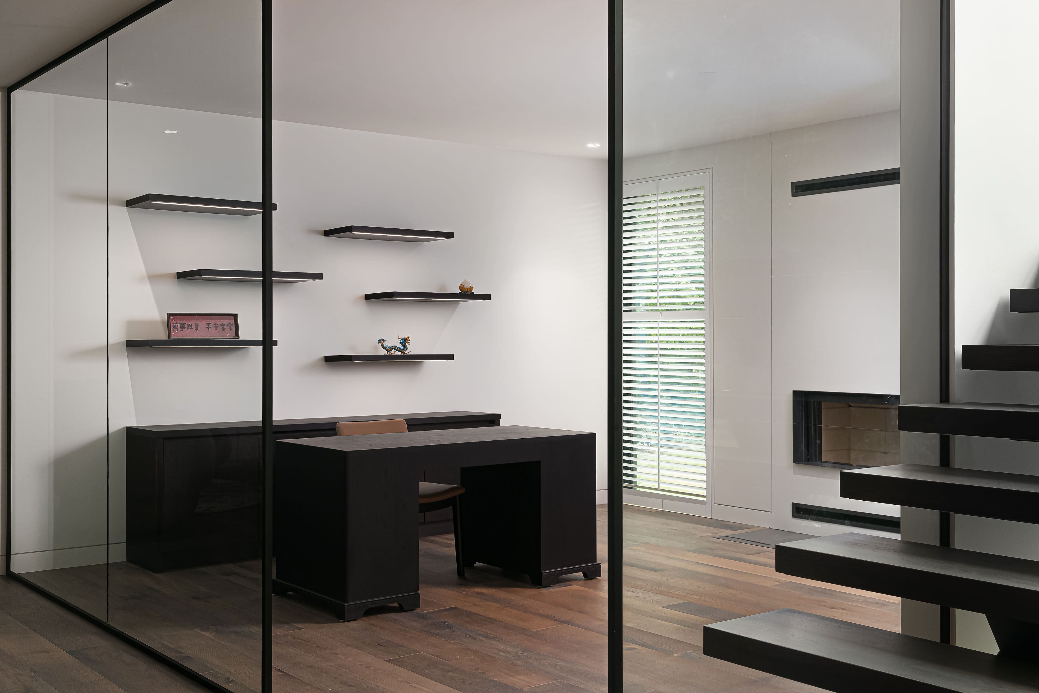Modern home office with custom black shelving, desk, and open staircase, featuring Goosen Inc.'s sleek millwork and minimalist design.