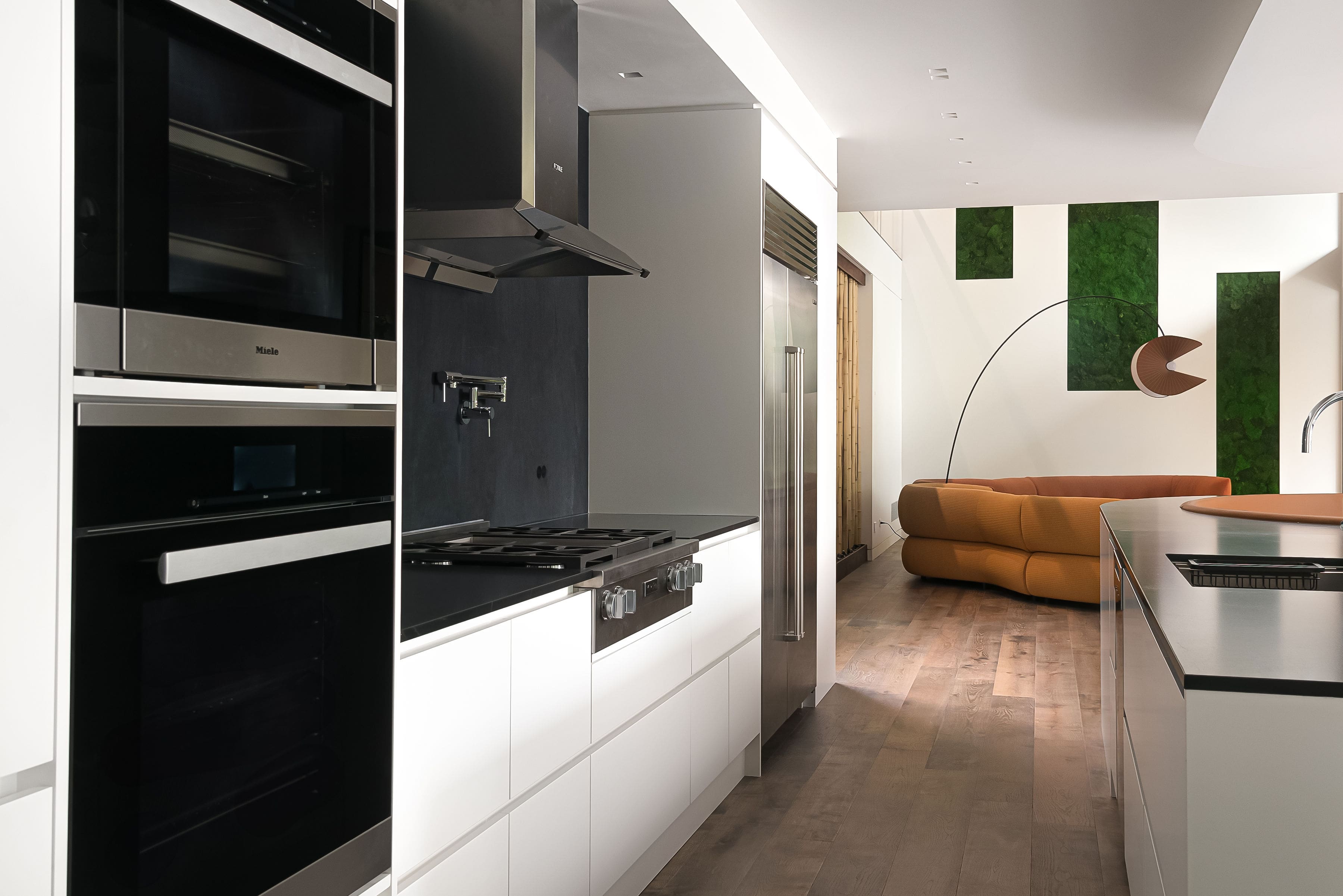 Contemporary kitchen with built-in appliances, white cabinetry, and open layout leading to a stylish living area, featuring Goosen Inc.'s custom millwork.