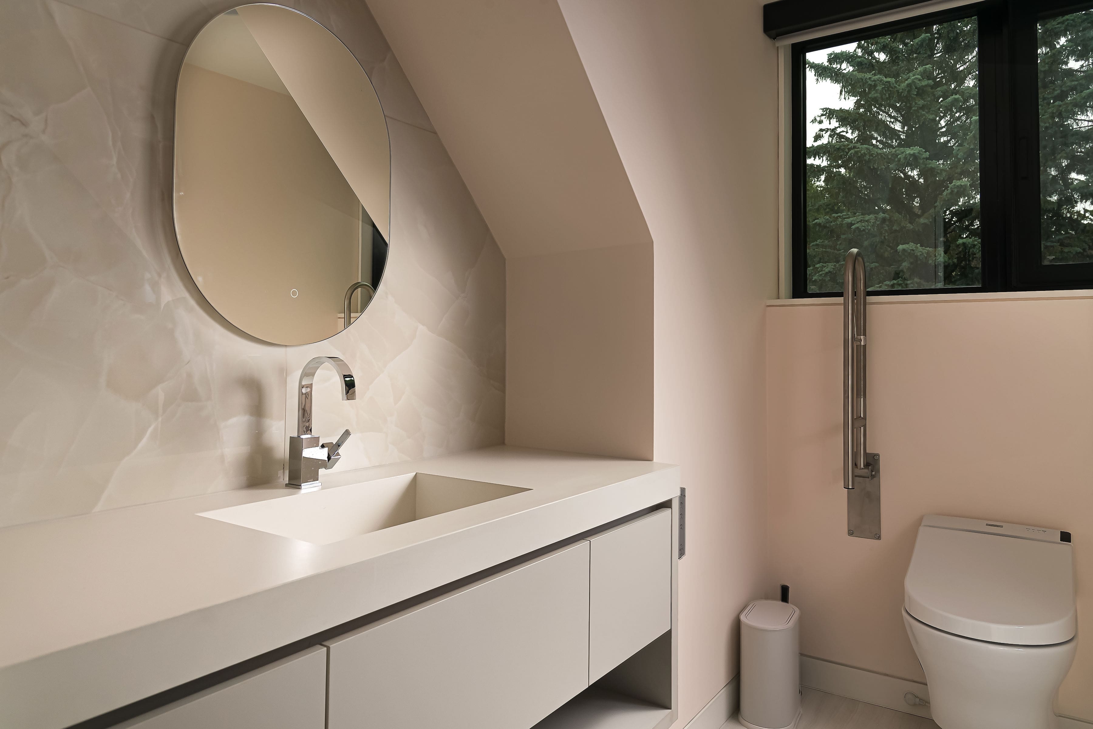 Modern bathroom with minimalist vanity, round mirror, and sleek fixtures, featuring Goosen Inc.'s custom cabinetry and refined millwork.