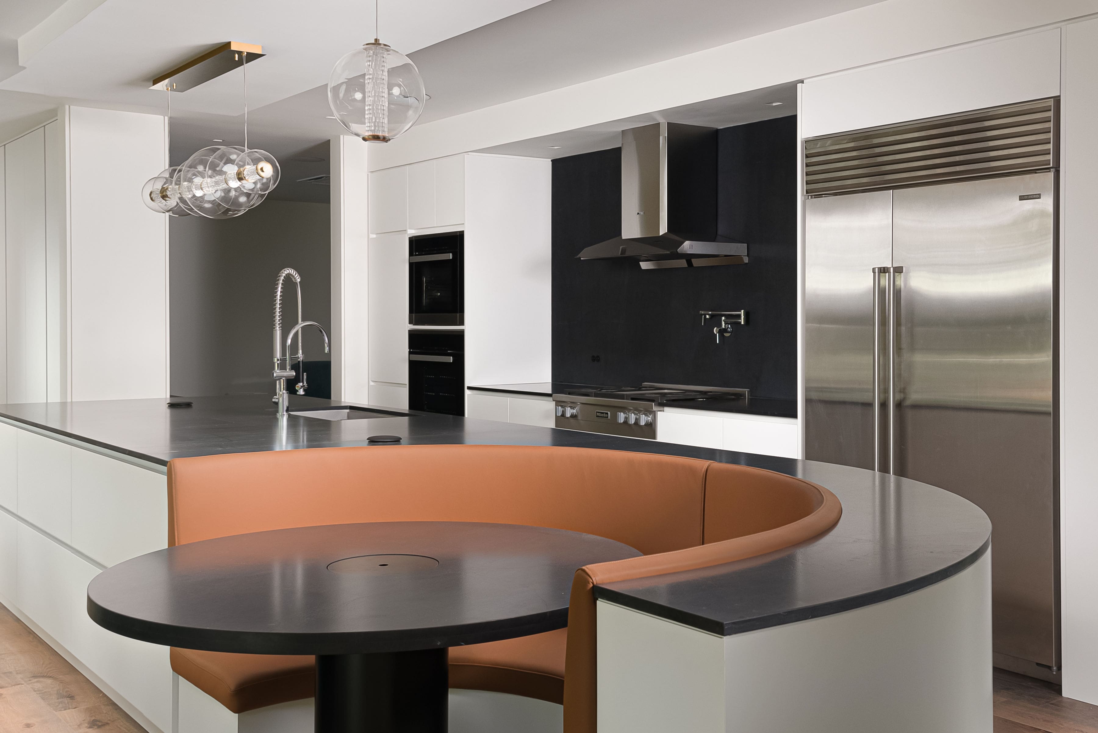 Modern kitchen with custom millwork featuring a curved built-in booth, black countertops, and pendant lighting.