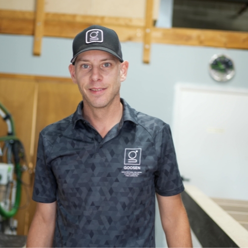 Goosen Inc. owner standing in a woodworking shop, wearing a branded shirt and cap.
