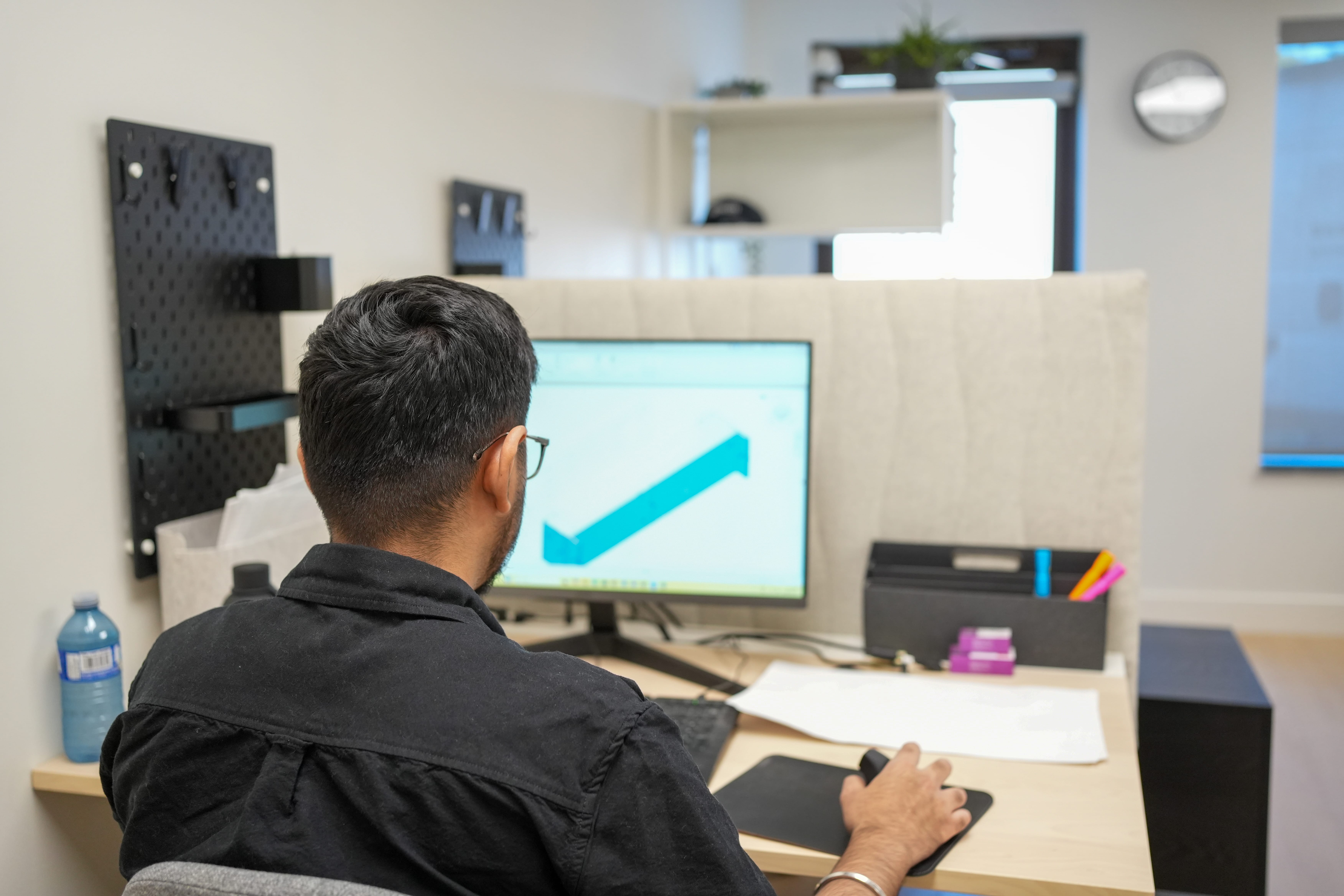 Architect working at a desk with interior design plans displayed on a computer monitor in a modern office.