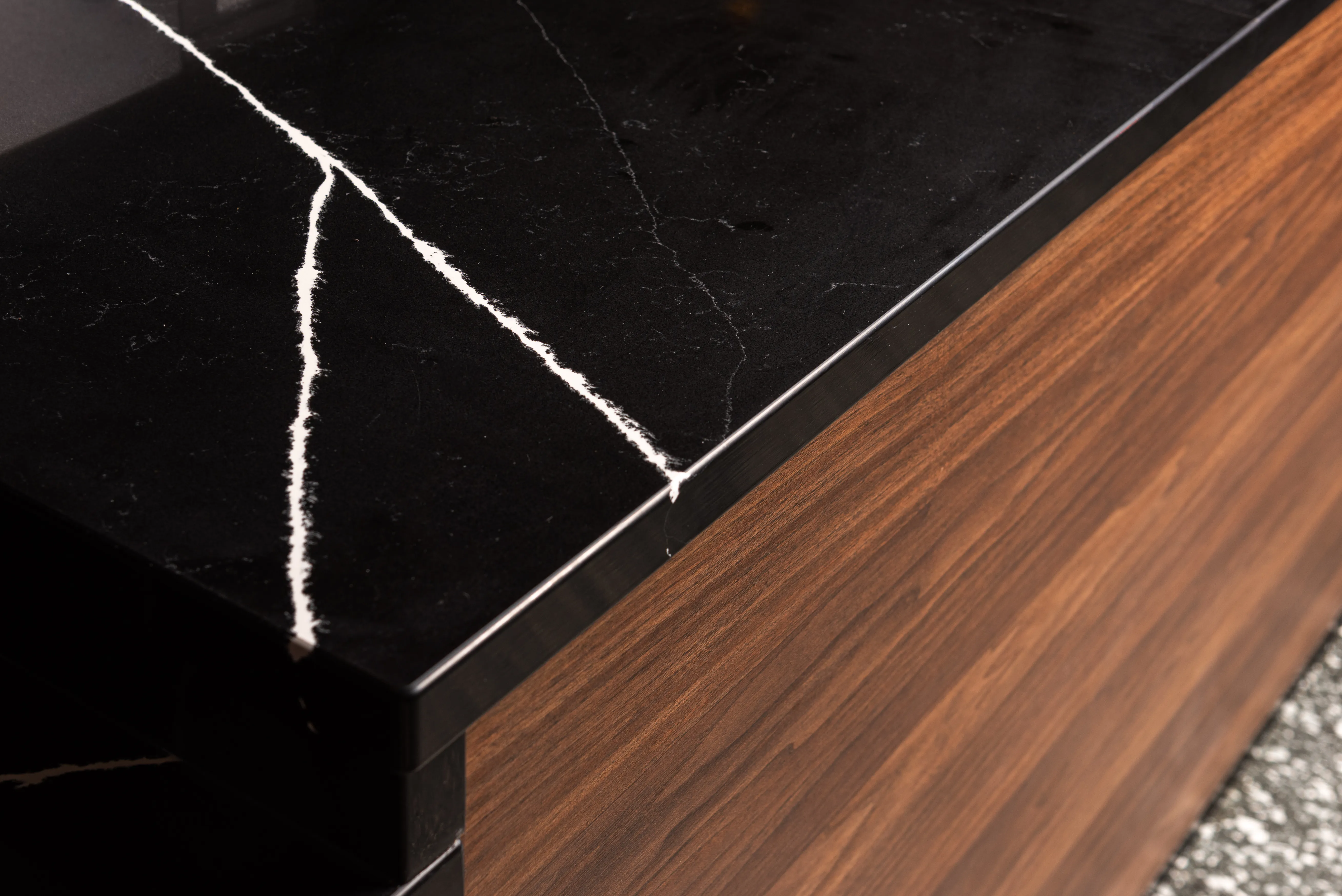 Close-up of black marble countertop with white veins and wood cabinetry below.