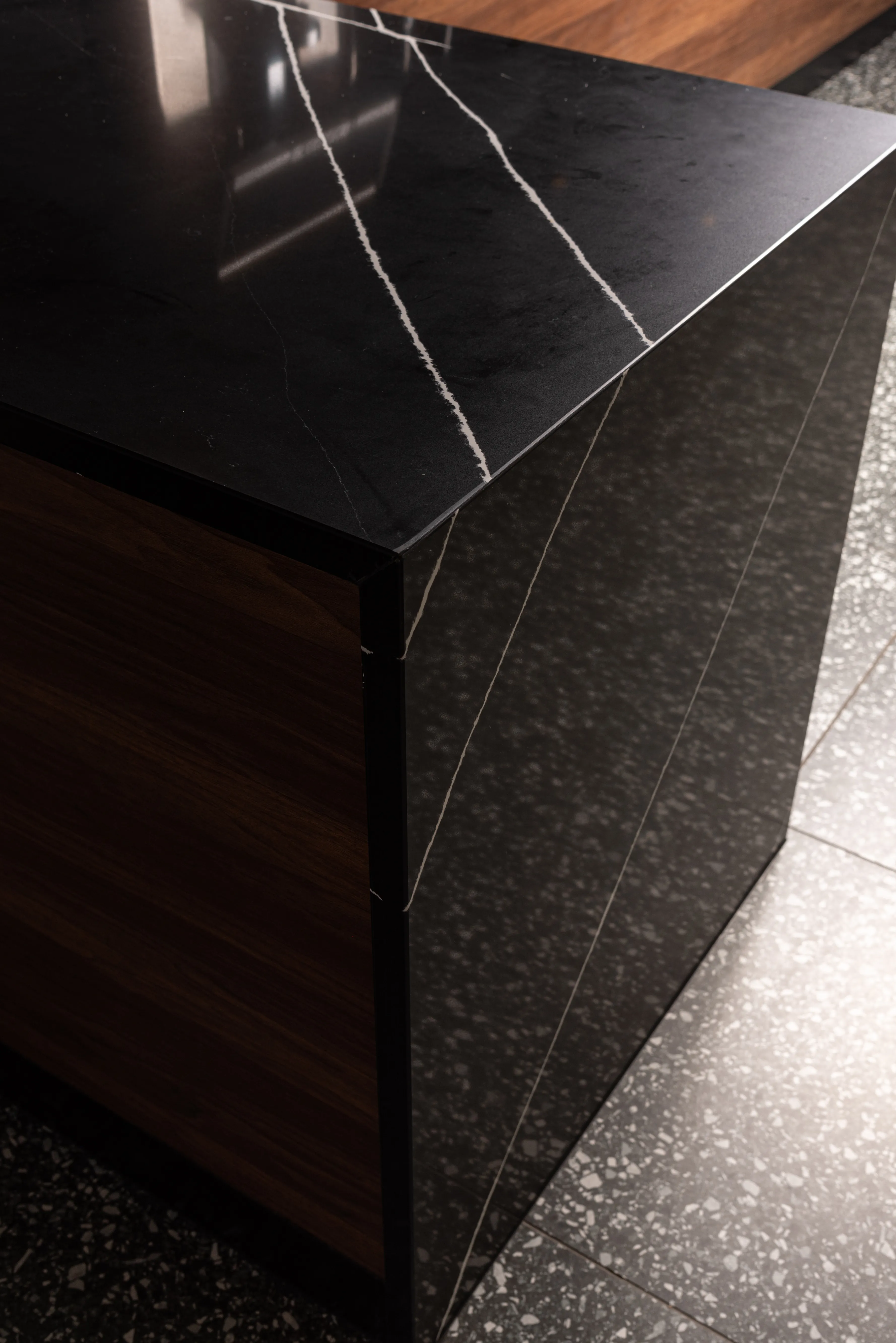 Close-up of a black marble table with white veins and a wooden side panel on a speckled floor.
