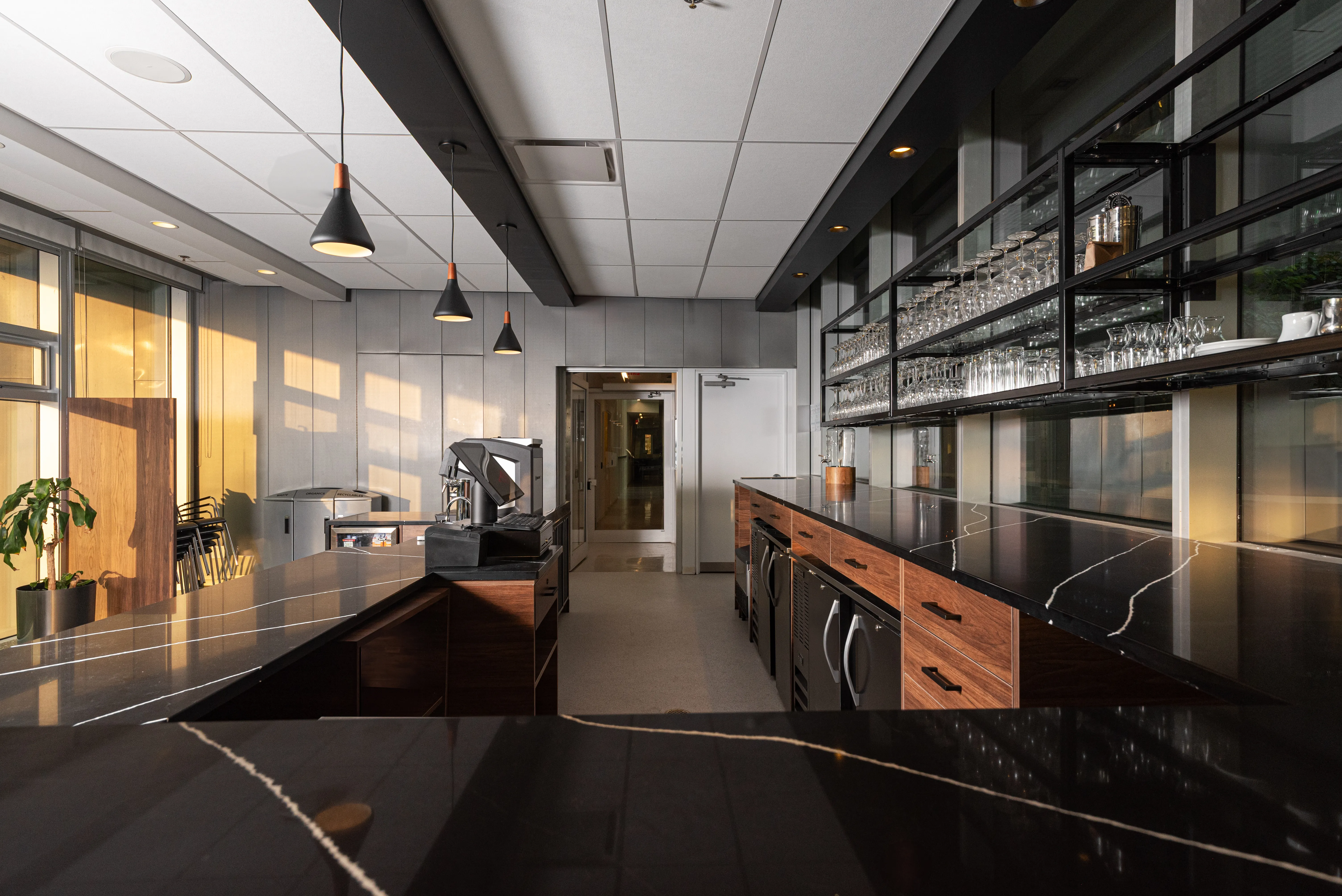 Modern bar area with black marble counters, wood cabinets, hanging lights, and shelves with glassware.