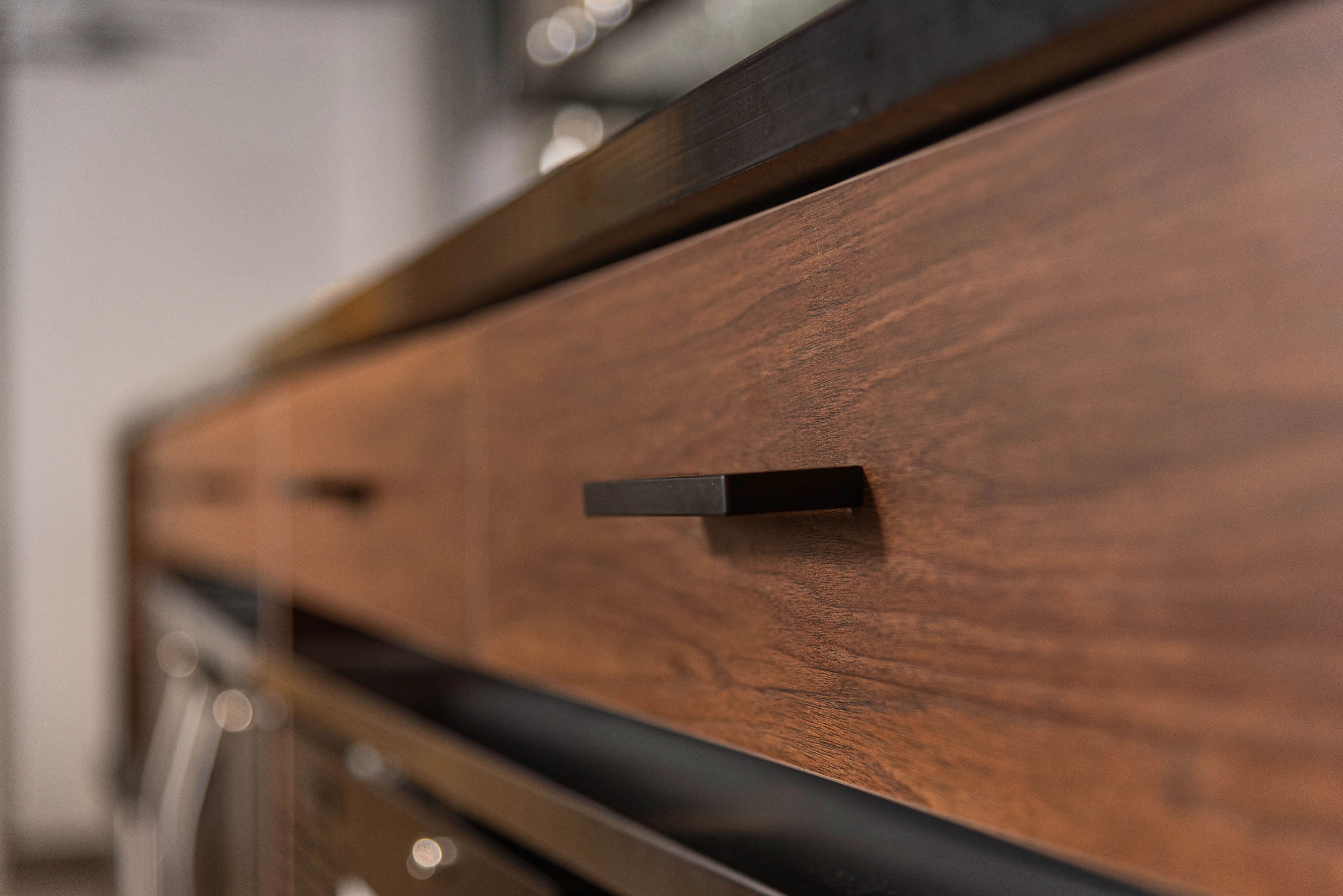 Close-up of a wooden kitchen cabinet drawer with a slim black handle.