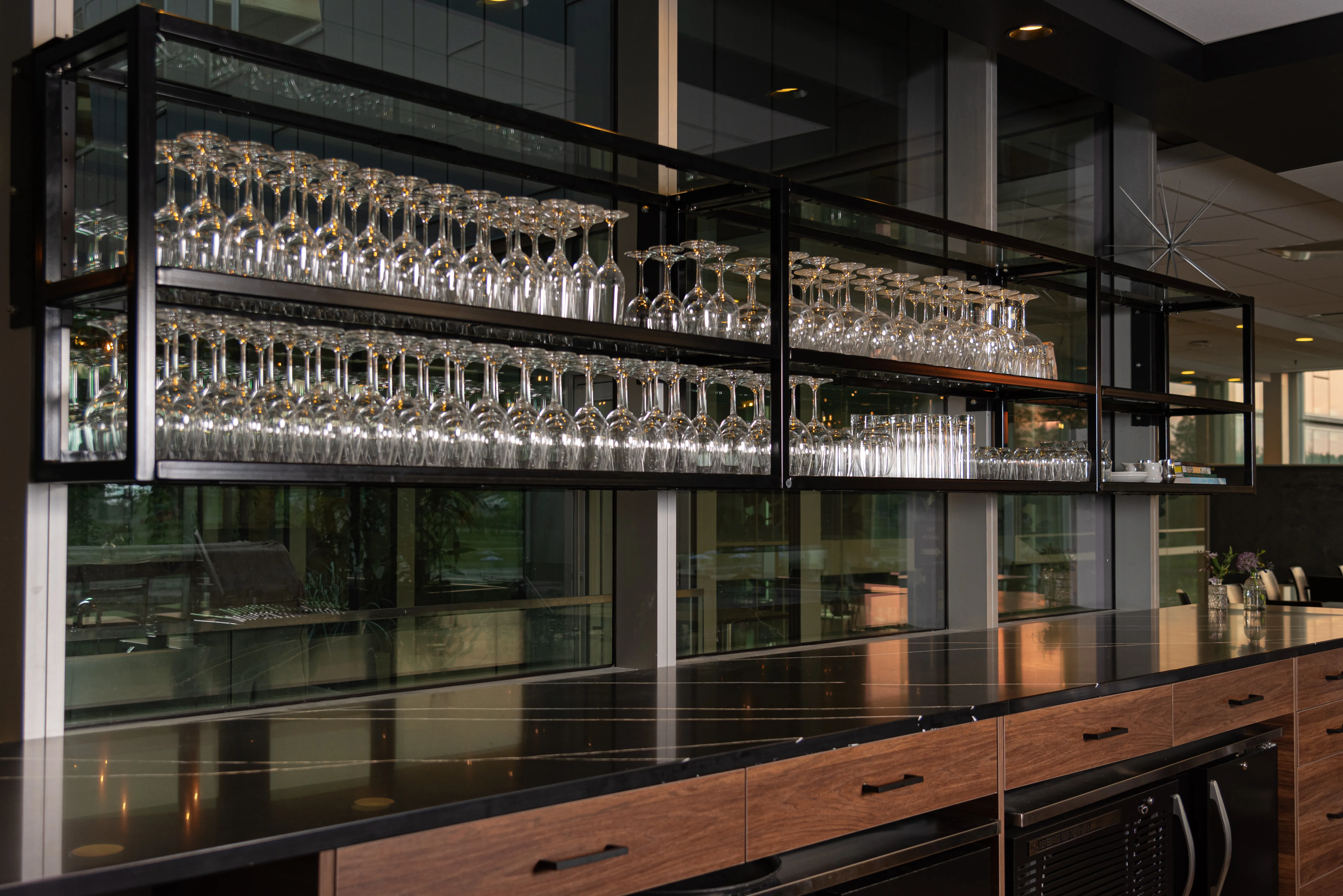 Modern bar counter with shelves holding rows of wine glasses and other glassware.
