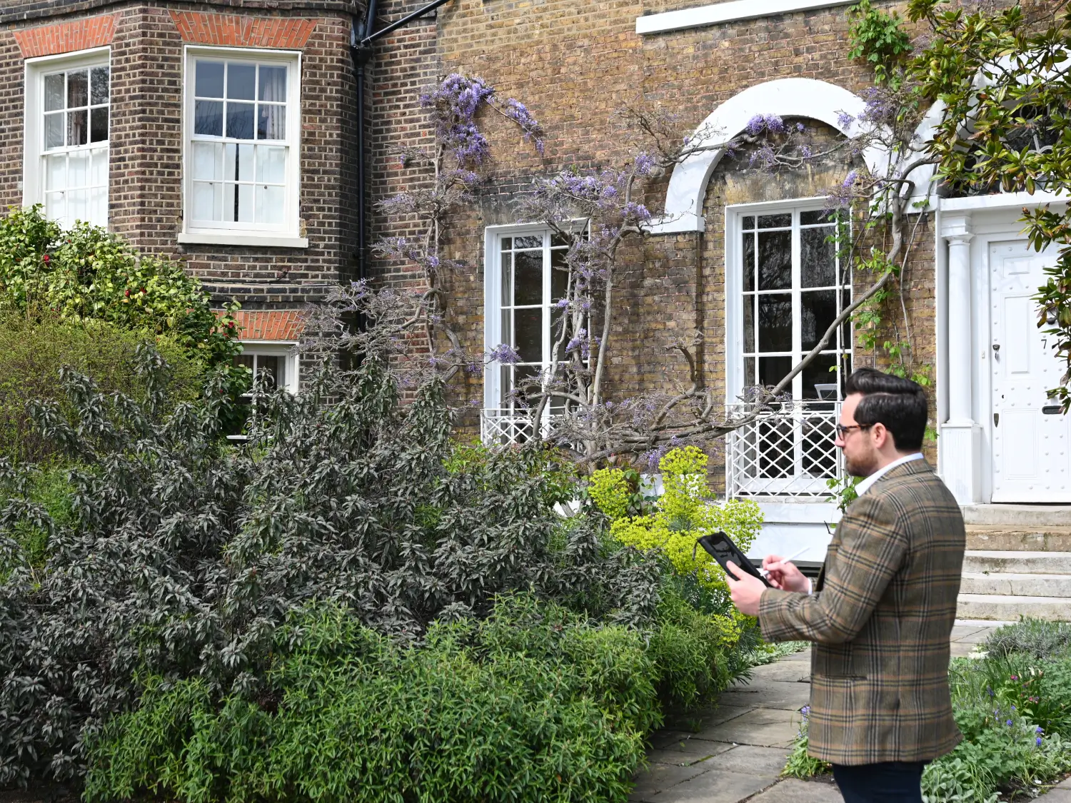 "Professional RICS surveyor conducting Schedule of Conditions inspection at period property in North London, documenting exterior condition with tablet device"