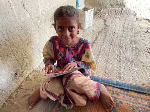 Small girl smiling, sits with workbook and pencil, 7-years-old Balochi student at Nosach English Language Center