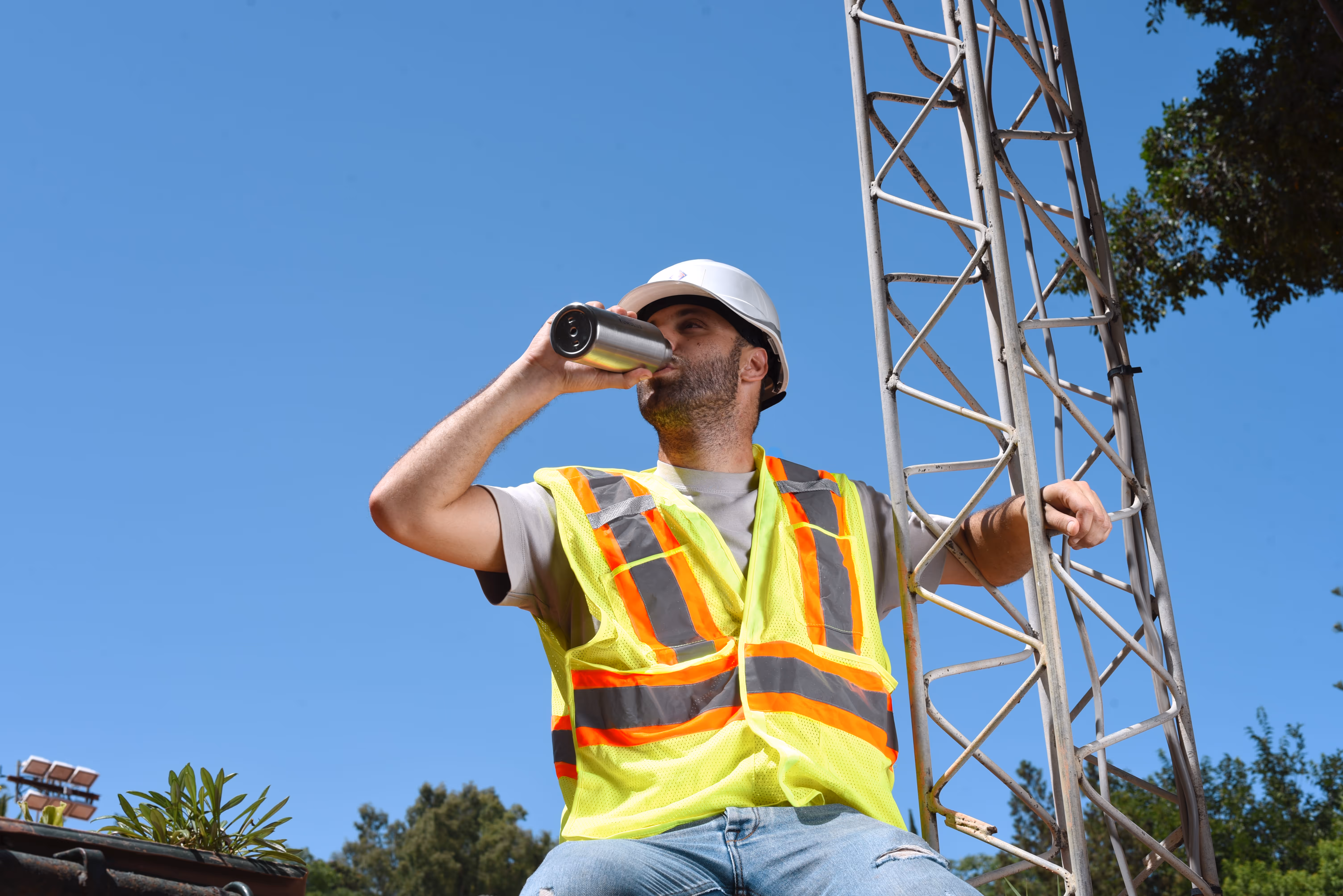 A man wearing a high-vis est on a construction site, drinking water from a Kumulus branded water bottle.