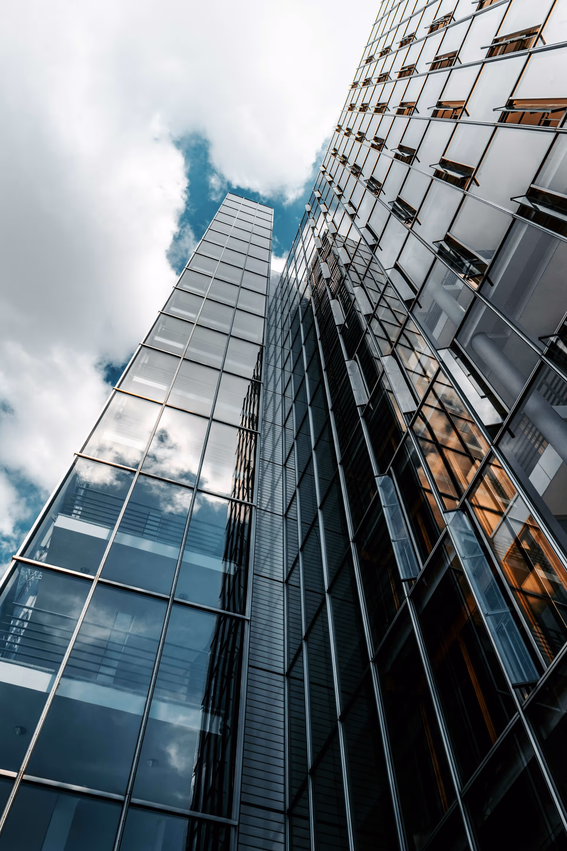 Low-angle view of tall glass office buildings reflecting clouds in the sky.