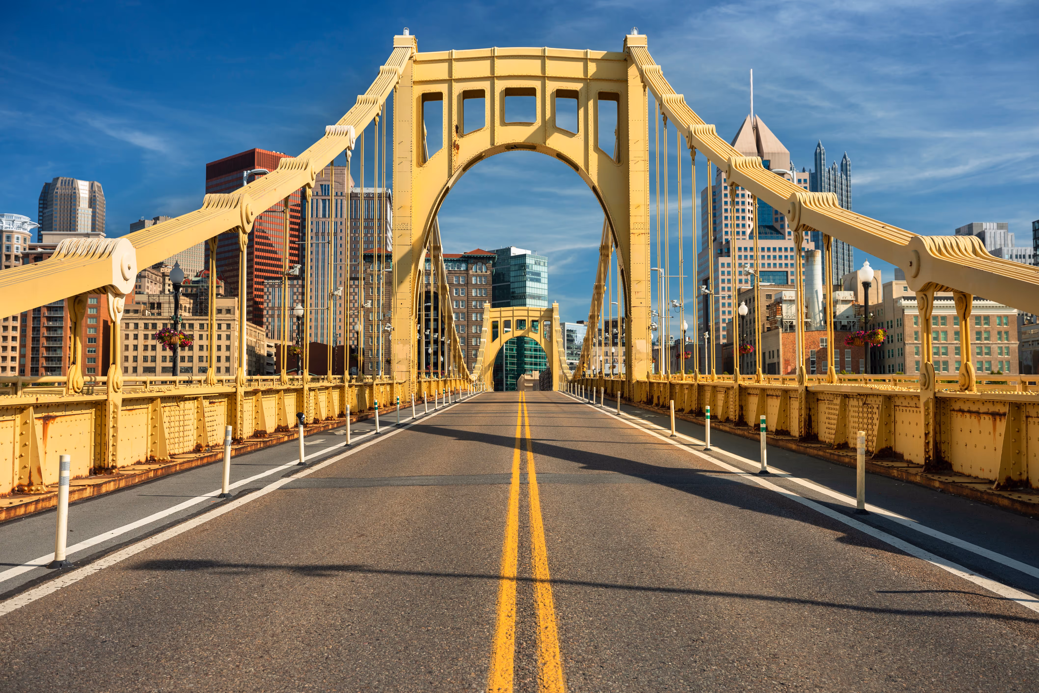 Empty yellow suspension bridge with city skyline in the background under a clear blue sky.