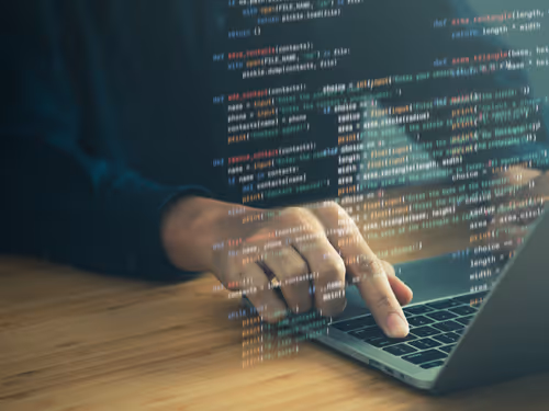 Person's hand typing on a laptop keyboard with overlaid programming code on the image.