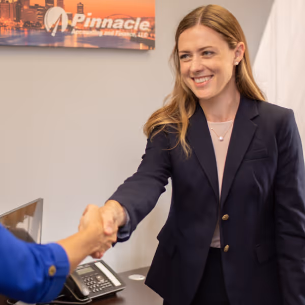 Smiling woman in business attire shaking hands with another person in an office setting.