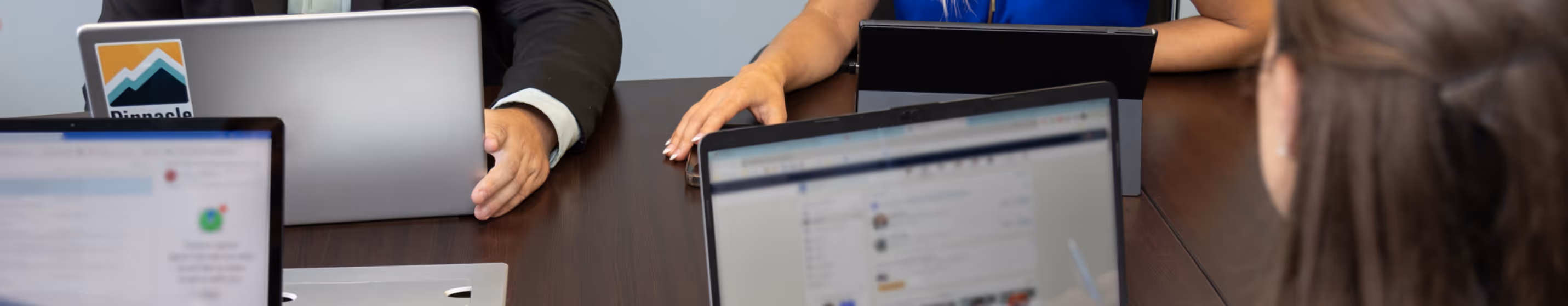 People sitting around a table working on laptops and tablets in a meeting.