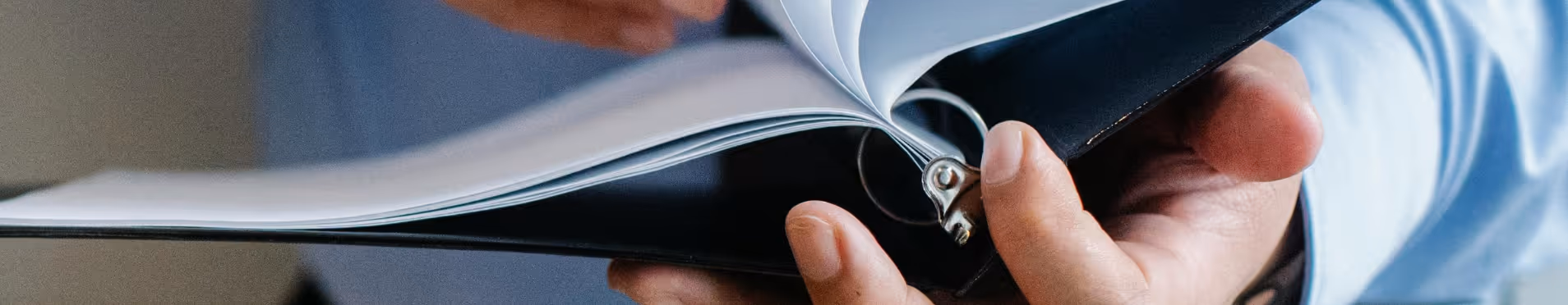 Close-up of a hand turning pages in a black ring binder with white papers.
