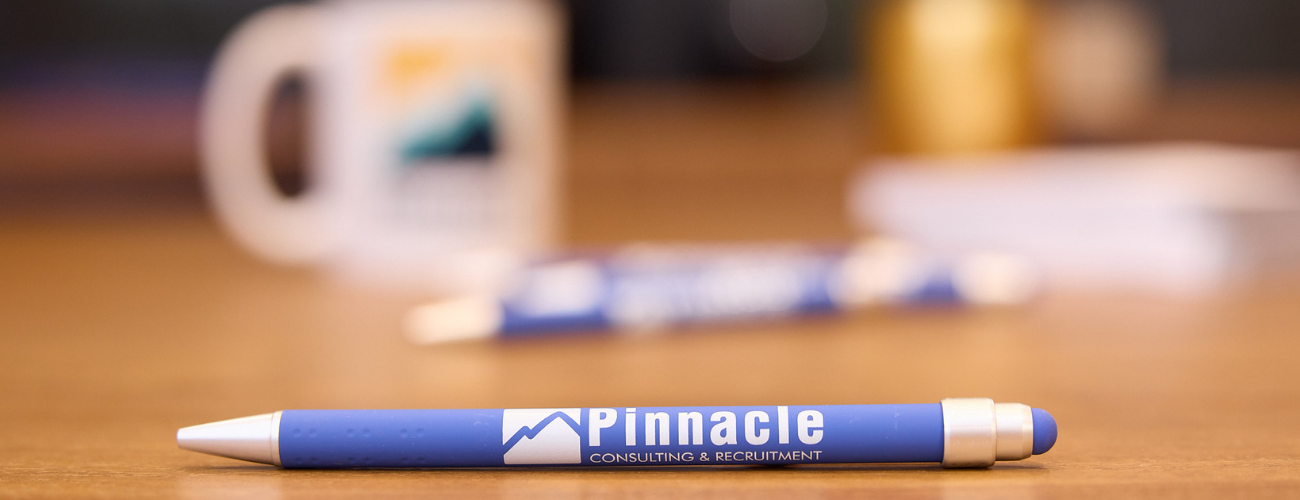 Desk phone with a screen displaying Pinnacle Consulting & Recruitment logo next to a small potted succulent plant.
